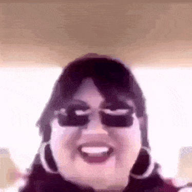 a close up of a woman wearing sunglasses and hoop earrings smiling .