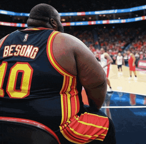 a man wearing a besong jersey sits in a chair watching a basketball game
