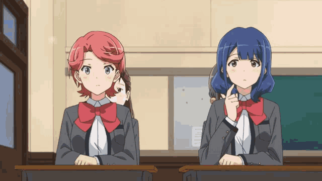 two anime girls are sitting at desks in a classroom looking at something