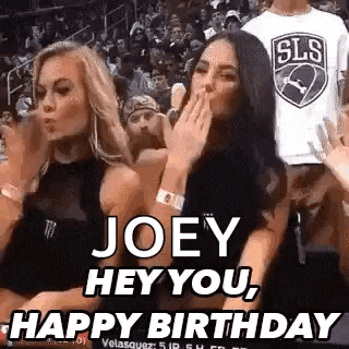 two women are sitting in the stands at a basketball game and one is blowing a kiss .