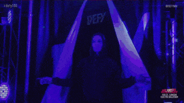 a woman in a black hoodie is standing in front of a sign that says ' defy ' on it .