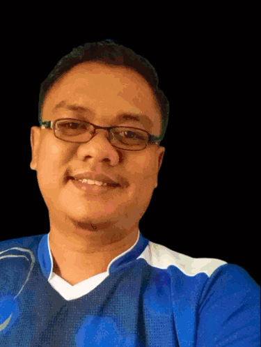 a man wearing glasses and a blue shirt smiles for a picture