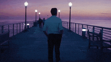 a man in a white shirt is walking down a pier at night