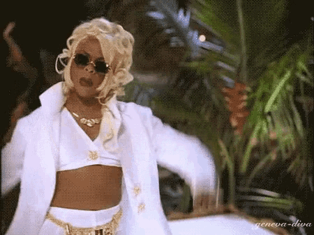 a woman in a white coat and crop top is dancing in front of a palm tree .