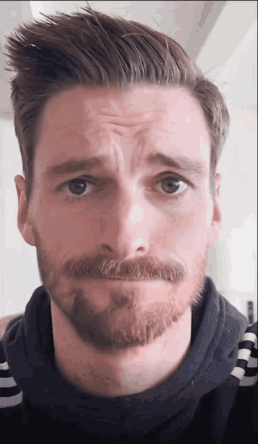 a man with a beard and a striped shirt makes a funny face