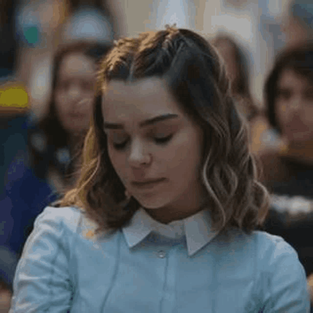 a woman in a blue shirt and white collar is sitting in a crowd of people .
