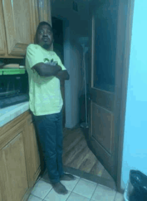 a man in a yellow shirt is standing with his arms crossed in a kitchen