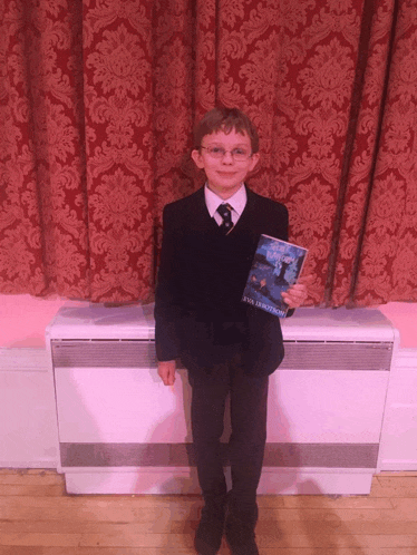 a young boy in a suit holds a copy of a book written by eva dunnett