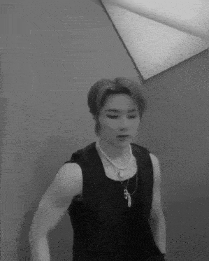 a black and white photo of a young man wearing a vest and a necklace .