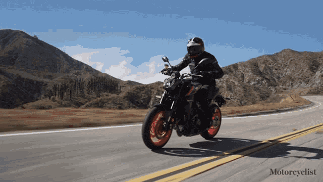 a man is riding a motorcycle down a road with mountains in the background and the word motorcyclist on the bottom