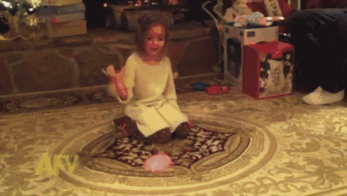 a little girl is kneeling on a rug in front of a fireplace with a box that says ' disney ' on it