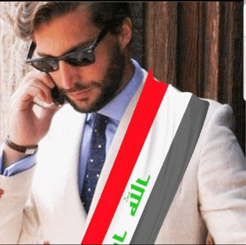 a man in a suit talking on a cell phone with a scarf that says iraq on it