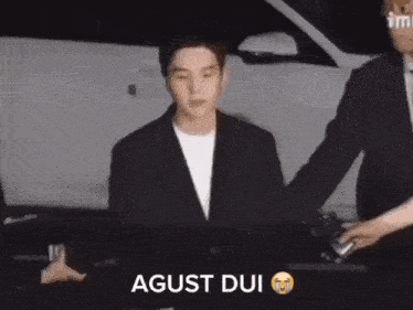 a man in a suit is being escorted by a man in a white shirt and the words agust dui are on the bottom