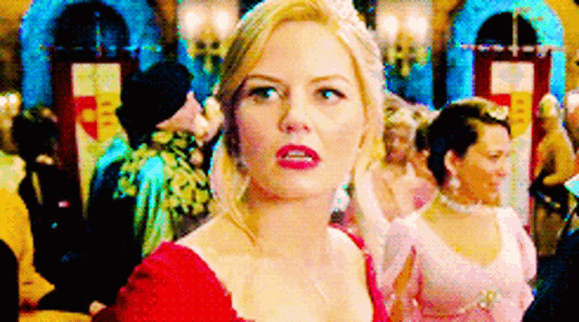 a woman in a red dress with a tiara on her head is standing in a crowd of people .