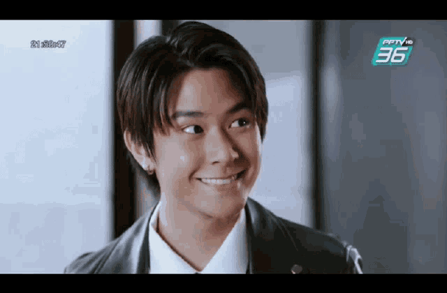 a young man in a leather jacket is smiling in front of a tv screen that says 36