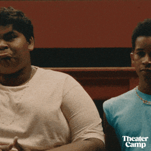 two men are sitting next to each other with the word theater camp on the bottom right