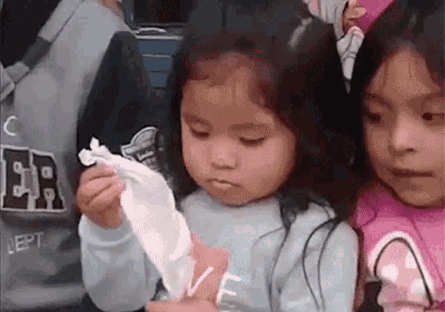 a little girl is holding a napkin in her hand while sitting next to another little girl .
