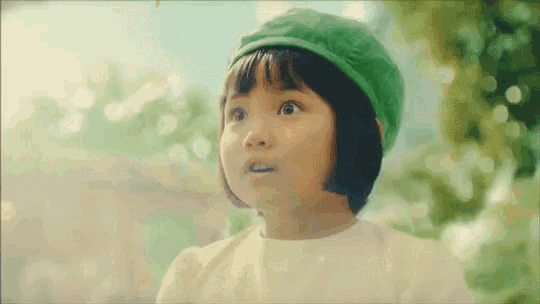 a little girl wearing a green hat and a white dress is looking up at something .
