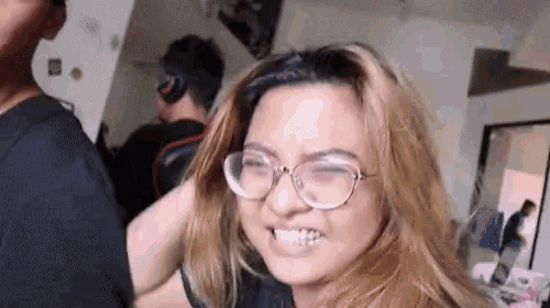 a woman wearing glasses is making a funny face in a room with other people .