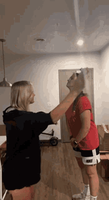 two women are standing next to each other in a room . one of the women is wearing a nike shirt .