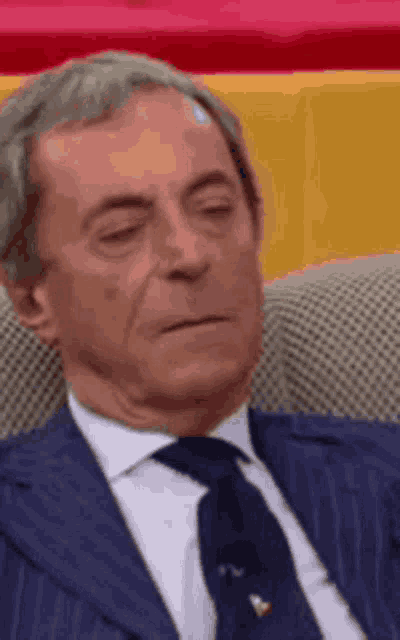 a man in a suit and tie is sitting in a chair with his eyes closed and his mouth open .