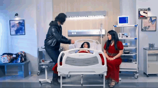 a woman in a red dress sits in a hospital bed next to a man in a black jacket and a sign that says sony