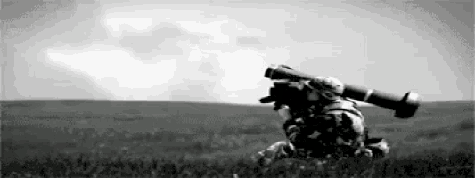 a black and white photo of a soldier carrying a missile in a field .