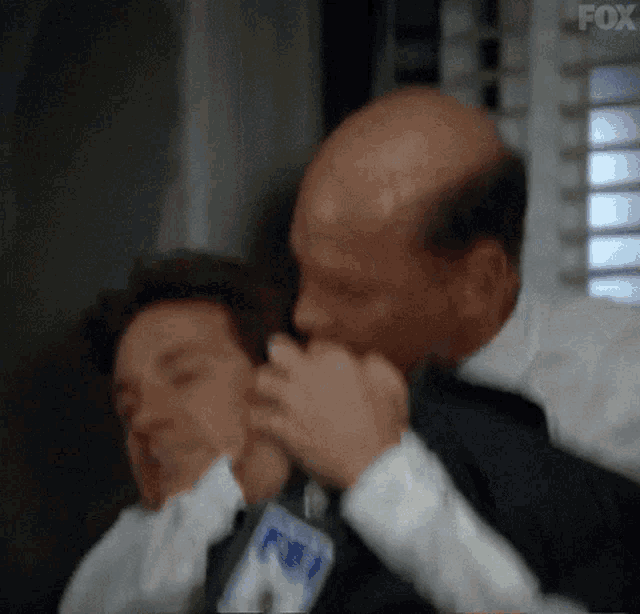 a man in a suit is holding another man 's neck in a room with a window in the background .