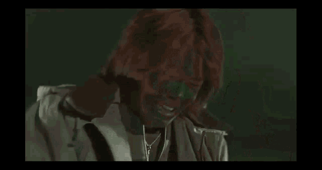 a person with green paint on their face is wearing a jacket .