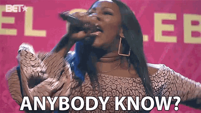 a woman is singing into a microphone with the words `` anybody know '' written on the screen behind her .
