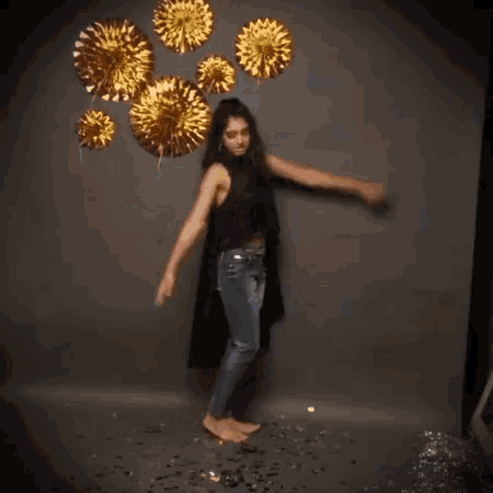 a woman is dancing in front of a wall holding gold decorations .