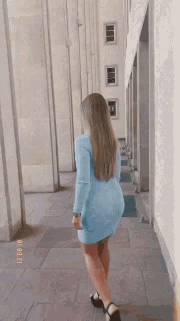 a woman in a blue dress walks down a hallway