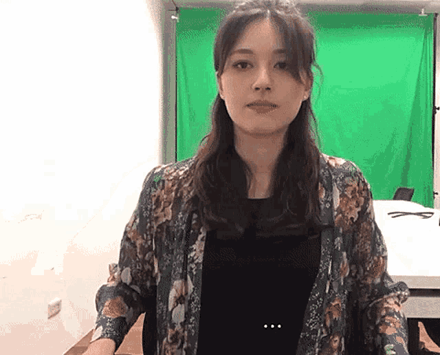 a woman is standing in front of a green screen looking at the camera