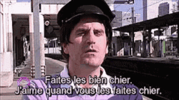 a man in a hat is standing in front of a train station and says faites les bien chier .