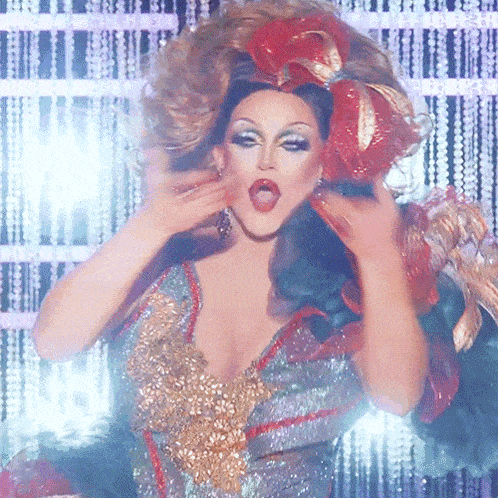 a drag queen is wearing a silver and gold dress and a red flower in her hair