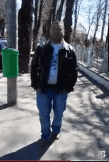 a man in a leather jacket and jeans is standing on a sidewalk