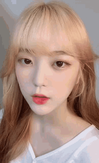 a young woman with blonde hair and red lips is wearing a white shirt and looking at the camera .
