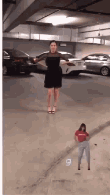 a woman in a black dress is standing in a parking garage next to a smaller woman in a red shirt with the number 9 on it