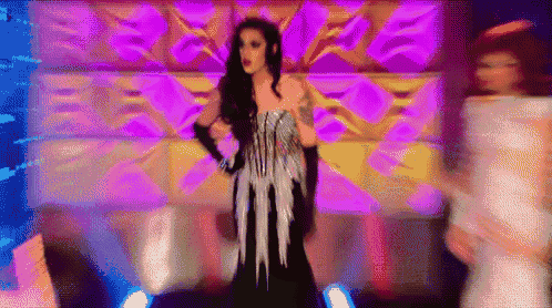 a drag queen is standing on a stage wearing a black and silver dress and gloves .