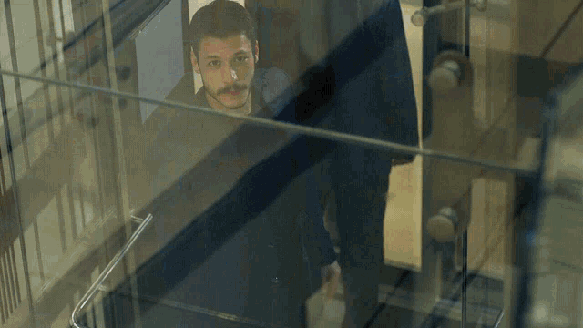 a man with a mustache is behind a glass wall
