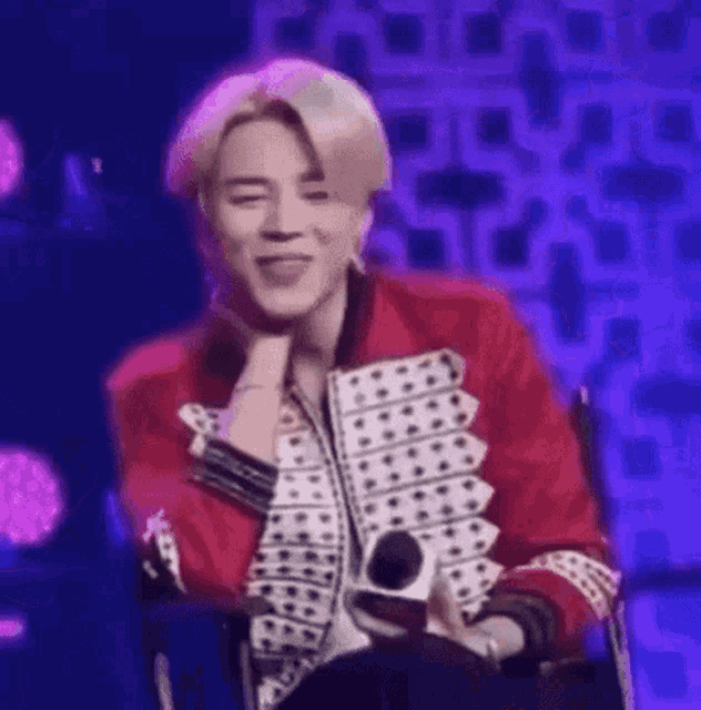 a man in a red jacket is sitting in a chair with a microphone in his hand .