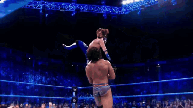 two men are wrestling in a ring and one of them is wearing a blue outfit with the number 10 on it .