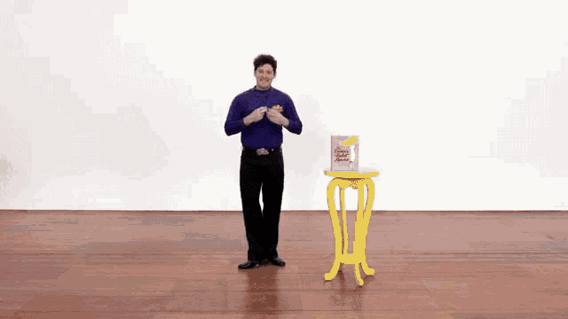 a man in a purple shirt is dancing next to a yellow table with a box of popcorn on it