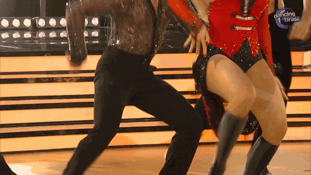 a woman in a red top and black shorts is dancing with a man in black pants on dancing brasil
