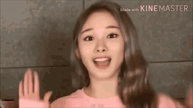 a woman in a pink sweater is waving her hand and smiling .