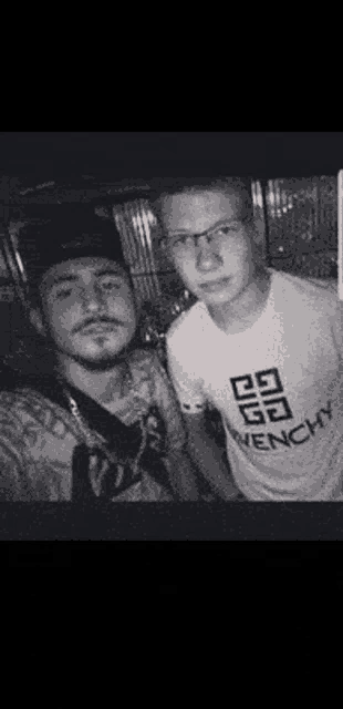 two young men are posing for a picture together . one of the men is wearing a givenchy shirt .