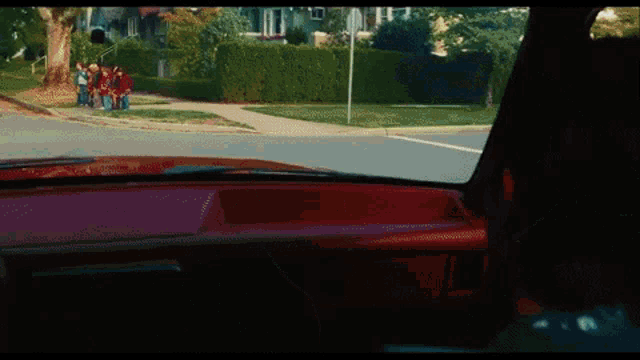 a red car is driving down a street with a group of people sitting on the sidewalk