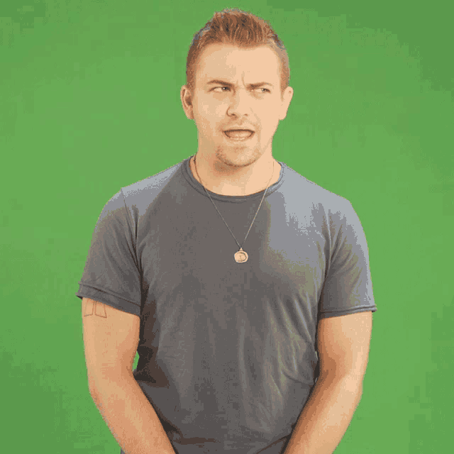 a man in a blue shirt with a necklace around his neck stands in front of a green screen