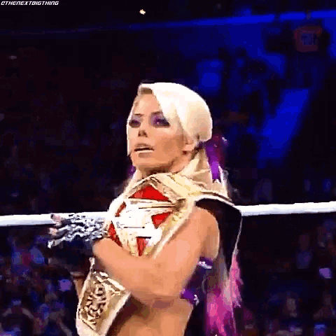 a woman is standing in a wrestling ring with her arms crossed and holding a championship belt .