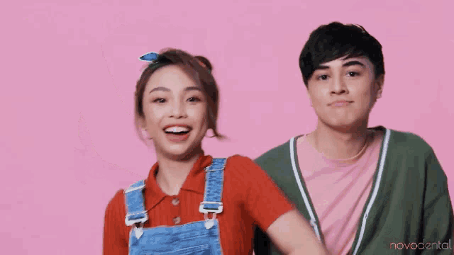 a man and a woman are standing next to each other and smiling on a pink background .